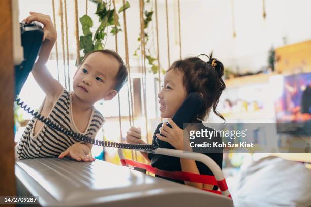 familienbindung und kinderentwicklung - asiatisch-chinesische geschwister, die spaß an rollenspielen mit einem traditionellen festnetztelefon haben - singapore school stock-fotos und bilder