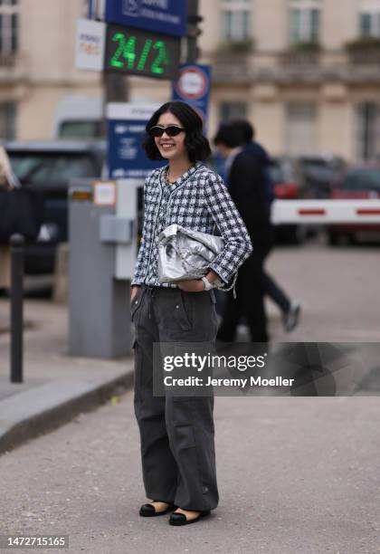 Fashion week guest seen wearing a tweed checked jacket, a silver bag, white shades, wide leg pants and ballet flats before the Chanel show on March...