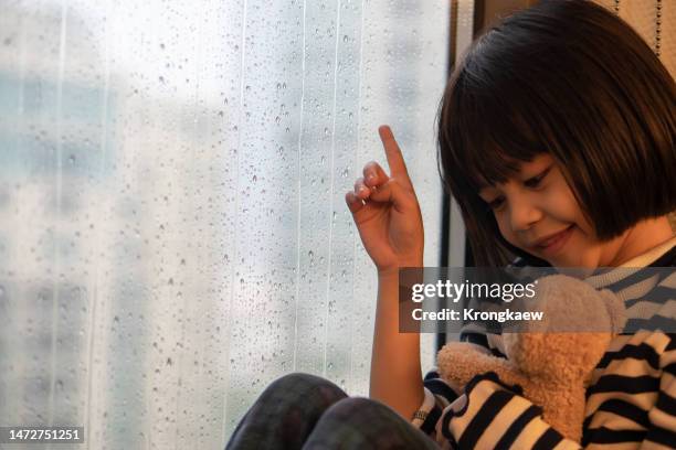 a girl sitting and talking with teddy bear on rainy day near glass window - storm outside window stock pictures, royalty-free photos & images