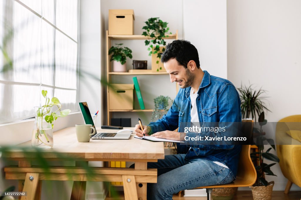 Young adult student man writing notes while using laptop to learn online. Education, e-learning and training course concept