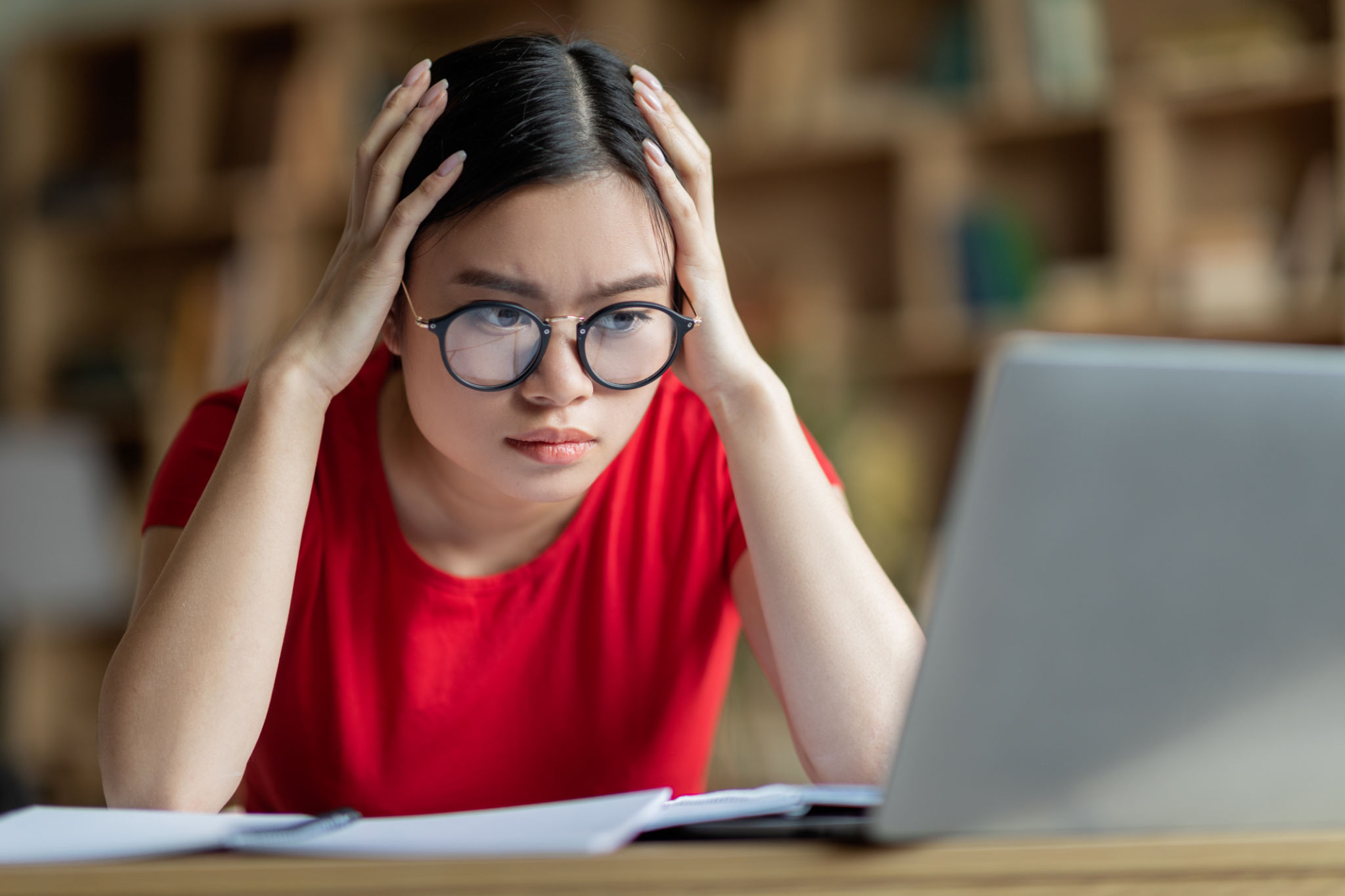 Concentrated busy young asian girl in glasses hold head with hands, look at computer in room interior Concentrated busy young asian girl in glasses hold head with hands, look at computer in room interior