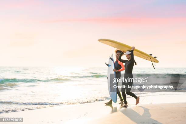 two young female surfers at the beach - beach hold surfboard stock-fotos und bilder
