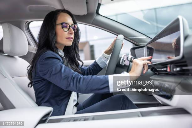 woman in business clothes touches the infotainment panel screen in her electric vehicle. - fahrerloses auto stock-fotos und bilder