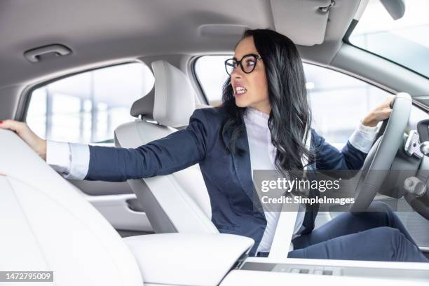 unexperienced driver with frightened facial expression reverses car looking over her shoulder. - reversing stock pictures, royalty-free photos & images