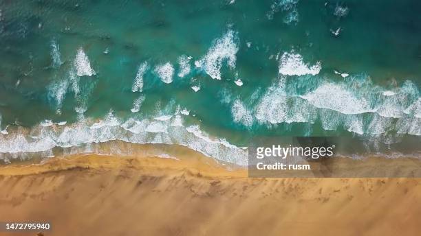 overhead aerial view of ocean waves splash against desert sand beach playa de cofete, jandia peninsula on fuerteventura, canary islands, spain - costas imagens e fotografias de stock