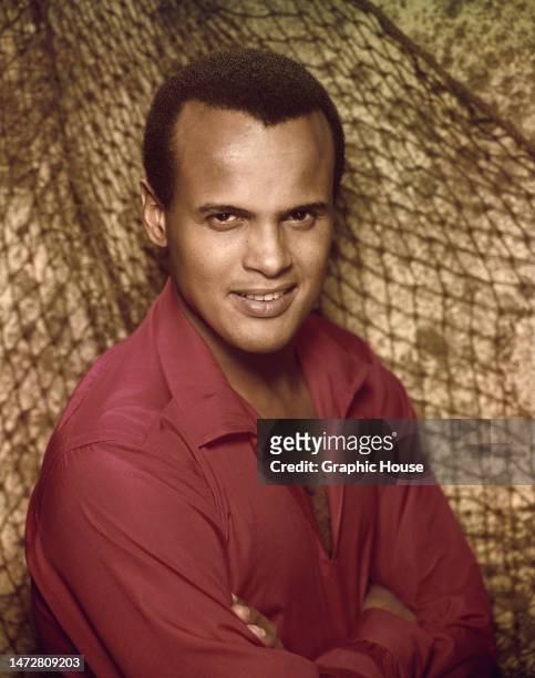 American singer, actor and civil rights activist Harry Belafonte wearing a pink shirt, with a fishing net in the background, United States, circa...