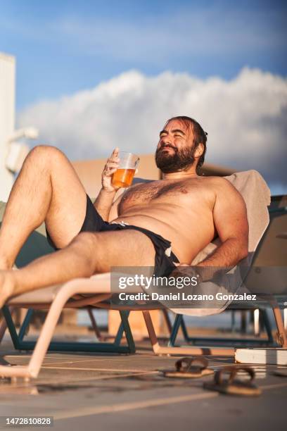 man lying on a sun lounger drinking beer at pool - islas baleares stock pictures, royalty-free photos & images