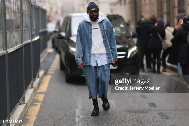 Jean-Claude seen wearing a dark beanie, black shades, a jeans jacket and matching jeans wide leg shorts, a white Jil Sander sweater, black boots and...