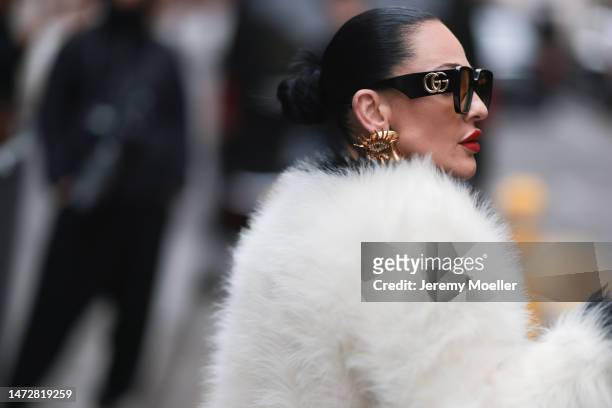 Fashion week guest seen wearing big golden earrings by Schiaparelli, black shades by Gucci, a fluffy white jacket and red lips before the Ottolinger...