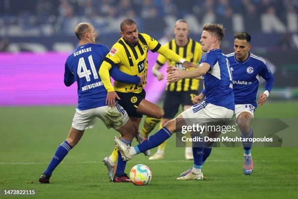 Donyell Malen of Borussia Dortmund is challenged by Henning Matriciani and Marius Buelter of FC Schalke 04 during the Bundesliga match between FC...