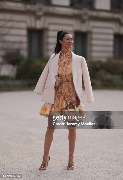 Amy Collins is seen wearing a golden Prada galleria bag, a colourful printed dress, an oversized blazer and high heels before the Zimmermann show on...