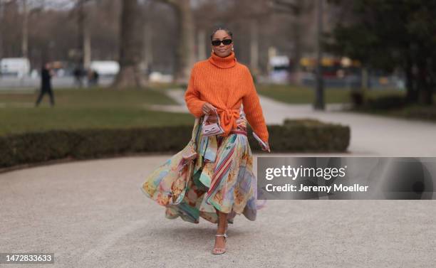 Ellie Delphine is seen wearing an orange turtleneck, a colourful skirt, high heels, dark sunglasses and a mini bag by Mach & Mach before the...