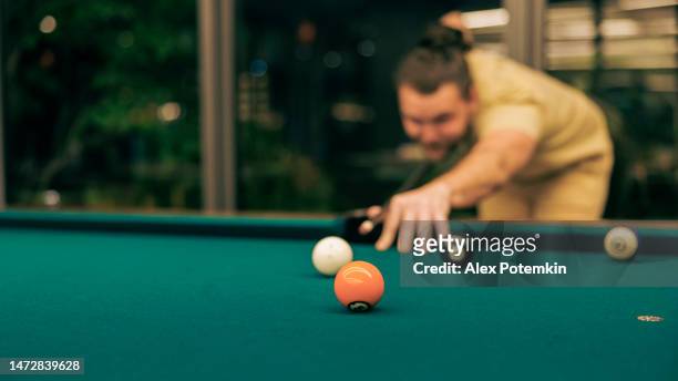 a player lines up a shot to sink the ball in a billiard bar. - sportsperson stock pictures, royalty-free photos & images