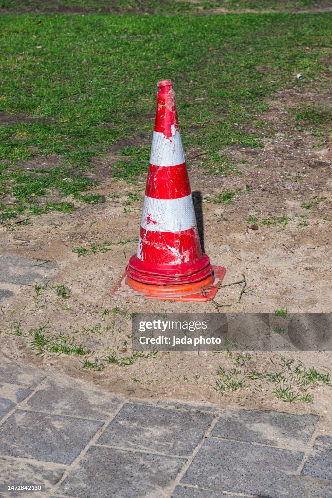 Three traffic cones stacked on top of each other standing on the sand near a lawn
