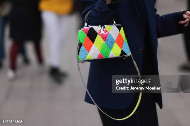 Fashion Week guest is seen wearing a pink, yellow, white and neon green fur Louis Vuitton bag with silver details and a dark blue blazer and black...