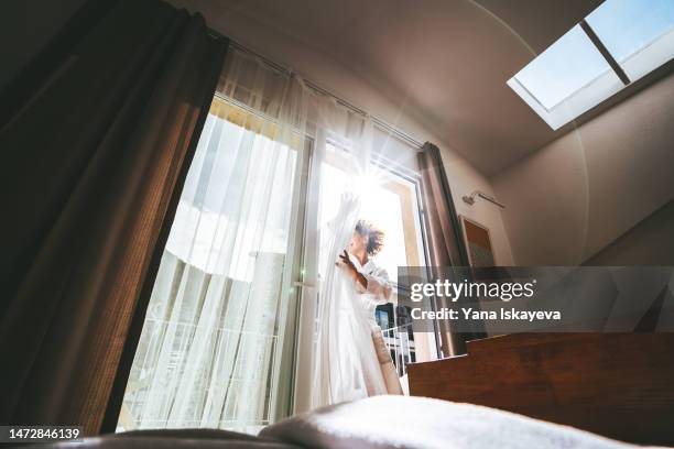 a happy woman opening curtains in a hotel room in the morning - curtain hotel stock-fotos und bilder