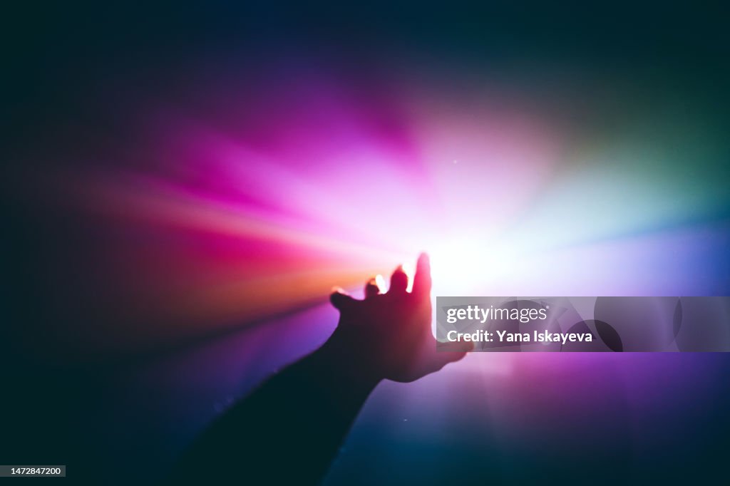 Intergalactic human journey concept with an arm reaching out to the bright vibrant multicolor light