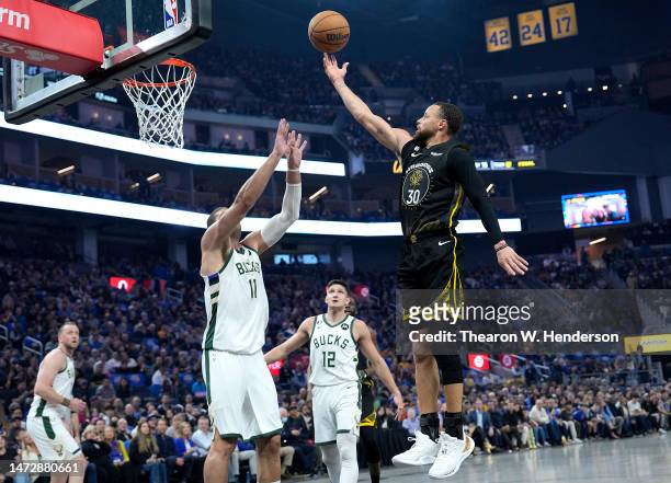 Stephen Curry of the Golden State Warriors shoots over Brook Lopez of the Milwaukee Bucks during the first quarter at Chase Center on March 11, 2023...