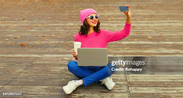 Stylish happy smiling young woman taking selfie with phone sitting with laptop in the city park on wooden floor background stylish happy smiling young woman taking