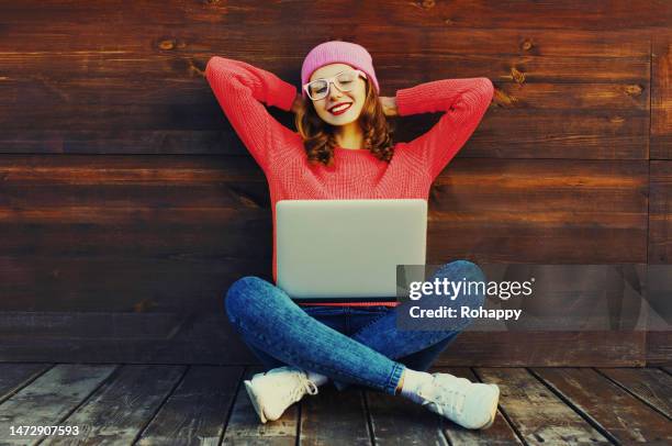 Portrait of stylish happy smiling young woman relaxing while working on laptop wearing a colorful clothes sitting on wooden floor in the city park portrait stylish happy smiling young woman
