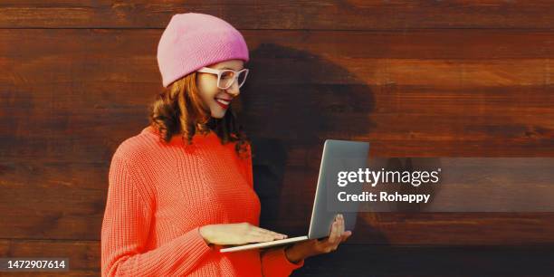 Portrait of stylish modern young woman working with laptop wearing colorful clothes outdoors on wooden wall background portrait stylish modern young woman working