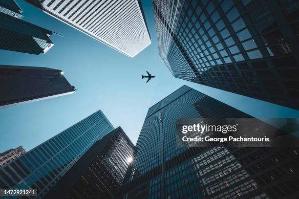 airplane flying over tall skyscrapers - finanzas globales fotografías e imágenes de stock
