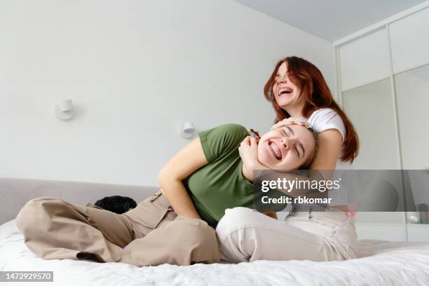 two happy teenage girls laughing and relaxing on the sofa at home - grimacing stock pictures, royalty-free photos & images