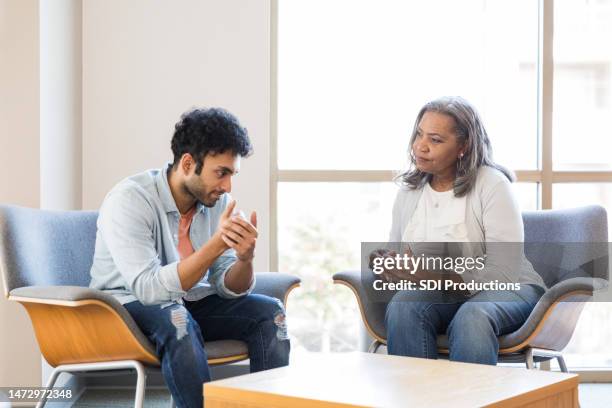 young adult male gestures while speaking with his mental health therapist - therapy stock pictures, royalty-free photos & images