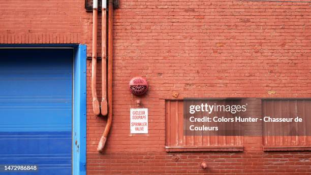 brick wall and windows painted and weathered in red with electric cables, wrinkled alarm, garage door and bilingual sign in montreal, quebec, canada - multilingual 個照片及圖片檔