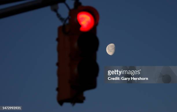 Percent illuminated waning gibbous moon sets behind a stoplight as the sun rises on March 12 in Union City, New Jersey.