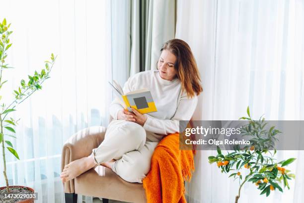 woman joying reading a book at home on weekends - curled up reading book stock pictures, royalty-free photos & images