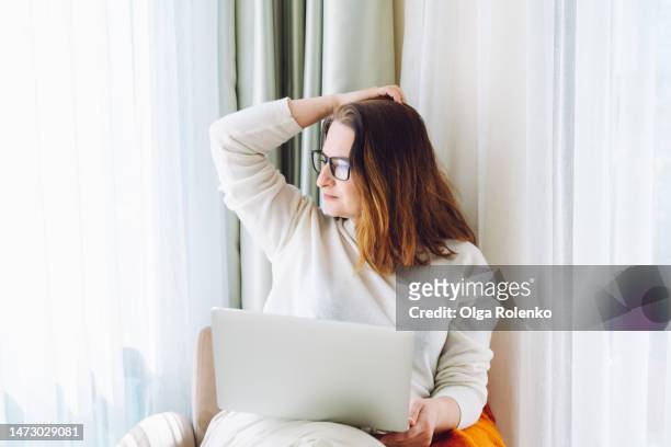 scriptwriter creative occupation. inspired woman with hand in hair work on laptop, looking out the window, thinking of new ideas - flexible working stock pictures, royalty-free photos & images