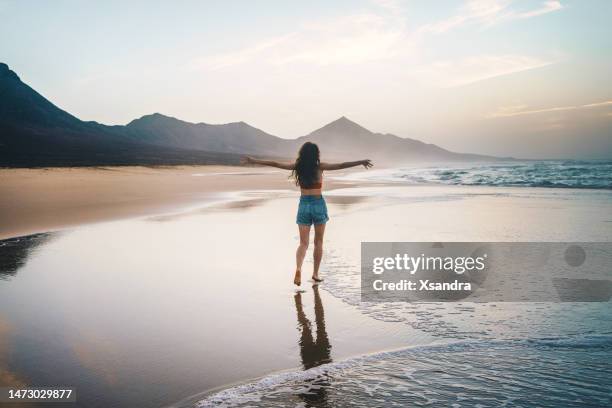 young woman walking alone on the beach at sunset - freedom and happiness concept - canarische eilanden stockfoto's en -beelden