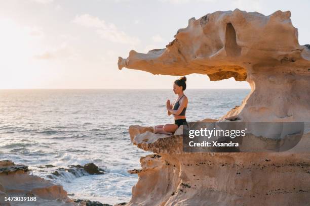 young woman meditating on a cliff overlooking an ocean - budismo imagens e fotografias de stock