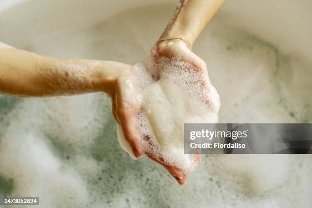 white toilet soap in female hands against the background of a fragrant foam bath. natural beauty, daily skincare routine. moisturizing, cleansing - woman bath bubbles stock-fotos und bilder