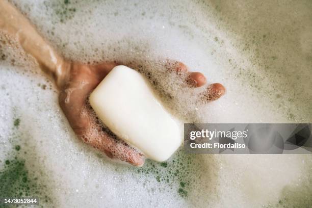 white toilet soap in female hands against the background of a fragrant foam bath. natural beauty, daily skincare routine. moisturizing, cleansing - soap suds stock pictures, royalty-free photos & images
