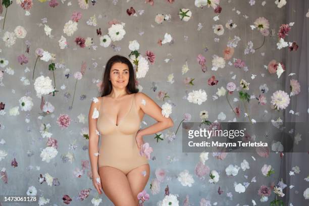 plus size woman in beige bodysuit surrounded by flowers. self acceptance. self love. imperfect body. beautiful girl. - chesty love stock pictures, royalty-free photos & images