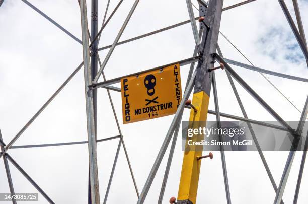 spanish-language sign stating 'peligro. alta tensión. no construir' [danger. high voltage. no building] on a steel electricity pylon carrying high tension power lines - peligro stock pictures, royalty-free photos & images