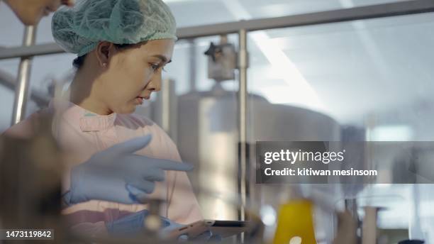 team nutritionist or quality control officer wear sterile clothing to prevent contamination, check production and product quality of juice filling machine in production line at manufacturing plant. employee work in bottled fruit juice factory. - food safety stock pictures, royalty-free photos & images