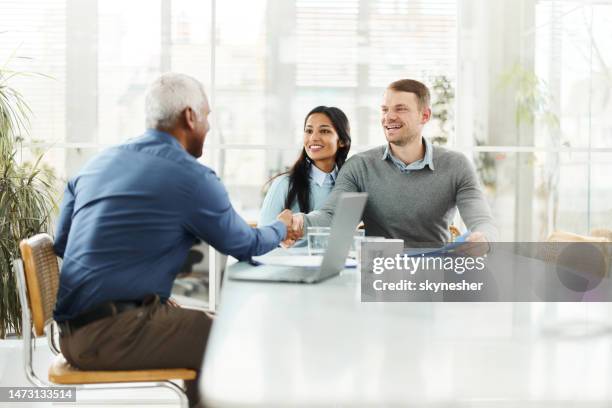 glückliches, vielfältiges paar, das dem versicherungsagenten im büro die hand schüttelt. - bank manager with client stock-fotos und bilder