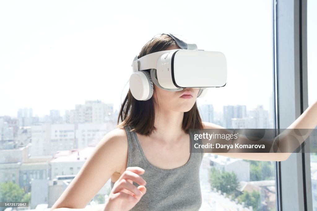 Young woman in VR helmet playing inside the modern room. Virtual reality glasses on the asian woman. The woman is mooving. Mockup for your design.