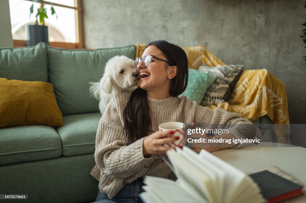 Junge Frau trinkt Tee, während sie zu Hause mit ihrem Hund spielt