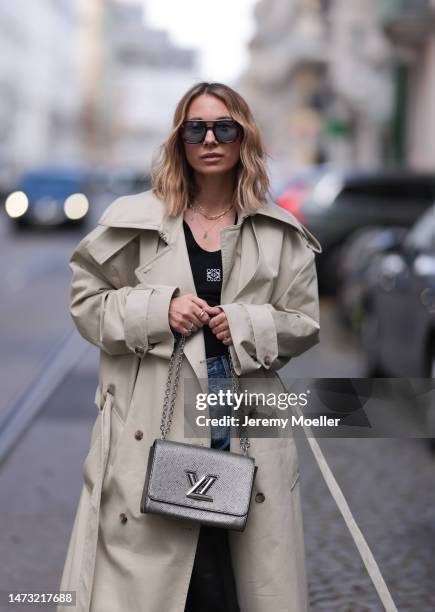 Karin Teigl seen wearing Andy Wolf brown sunglasses with blue lenses, gold jewelry, H&M beige oversize long trenchcoat, Loewe black logo top, Louis...