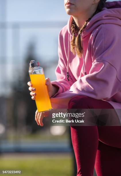 young woman is hydrating during outdoor exercise in public park. - energy drink stock pictures, royalty-free photos & images