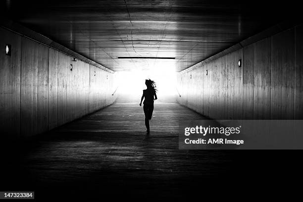 black amd white image of girl running towards the light - tunnel stock pictures, royalty-free photos & images