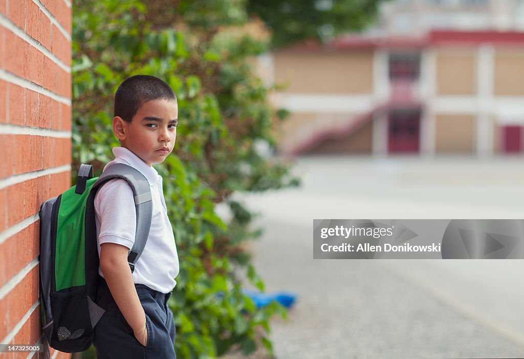 Schoolboy in uniform leaning against brick wall