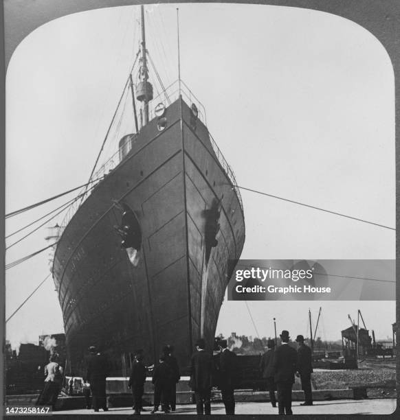 Group of people gathered on the dockside before the bow of RMS Lusitania, possibly at Pier 54, the Cunard pier, in New York harbour, New York City,...