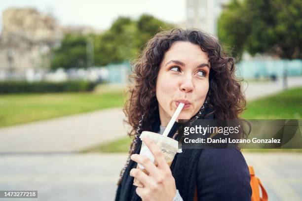 cool woman drinking iced coffee walking in a park - suck stock pictures, royalty-free photos & images
