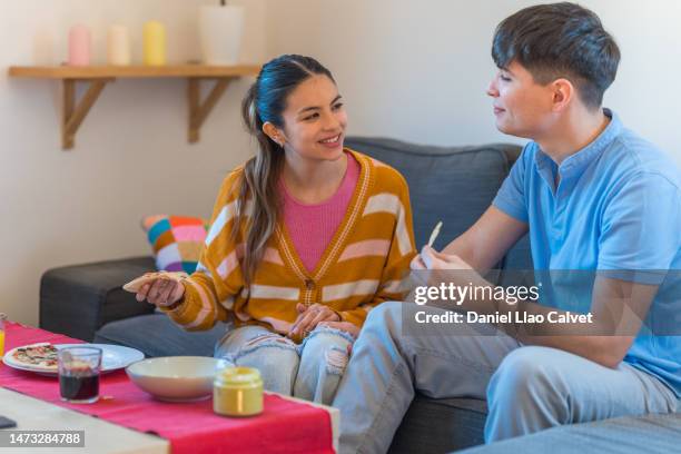 happy young couple sitting on couch eating pizza and nacho chips - casa calvet stock pictures, royalty-free photos & images