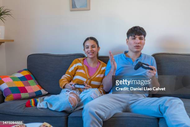 young couple, sitting on a couch and holding video game controls. - casa calvet stock pictures, royalty-free photos & images